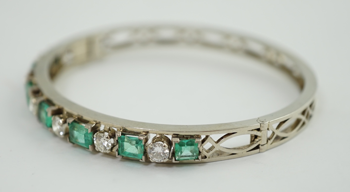 A modern 14k white gold, seven stone graduated emerald and six stone round cut diamond set hinged bangle